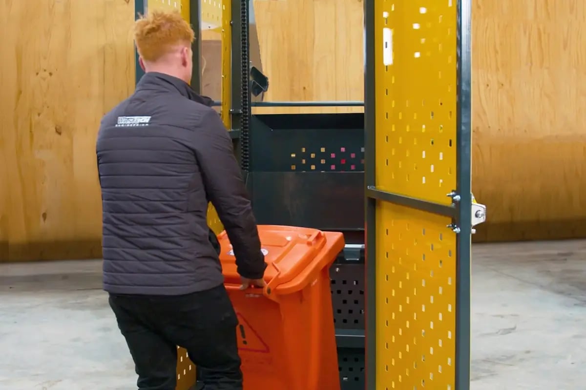 Operator loading a wheelie bin into the Wastech Slimline Bin Lifter access gate